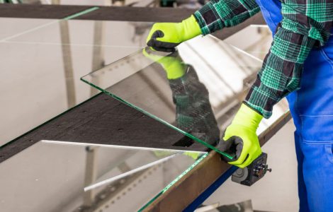 Un homme en combinaison bleu et gants jaunes coupant un panneau de verre