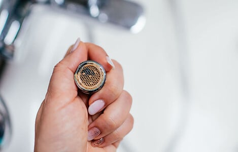 Focus sur la main d’une femme tenant le mousseur du robinet un peu rouillé