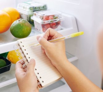 Une femme vérifie le réfrigérateur et fait la liste des courses sur un petit carnet