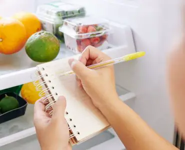 Une femme vérifie le réfrigérateur et fait la liste des courses sur un petit carnet