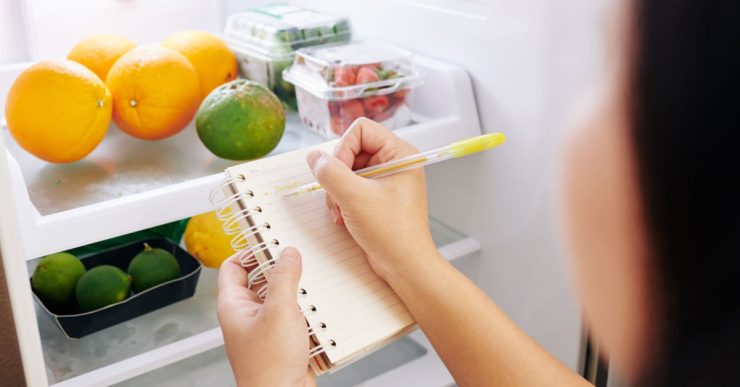 Une femme vérifie le réfrigérateur et fait la liste des courses sur un petit carnet