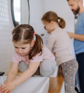 Un homme et deux petites filles se lavant les mains dans la salle de bain