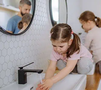 Un homme et deux petites filles se lavant les mains dans la salle de bain