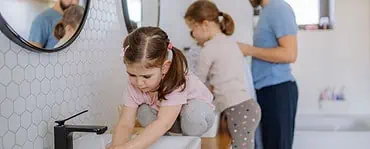 Un homme et deux petites filles se lavant les mains dans la salle de bain