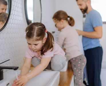 Un homme et deux petites filles se lavant les mains dans la salle de bain