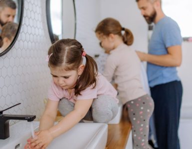 Un homme et deux petites filles se lavant les mains dans la salle de bain