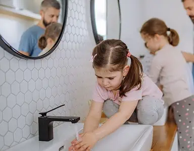 Un homme et deux petites filles se lavant les mains dans la salle de bain