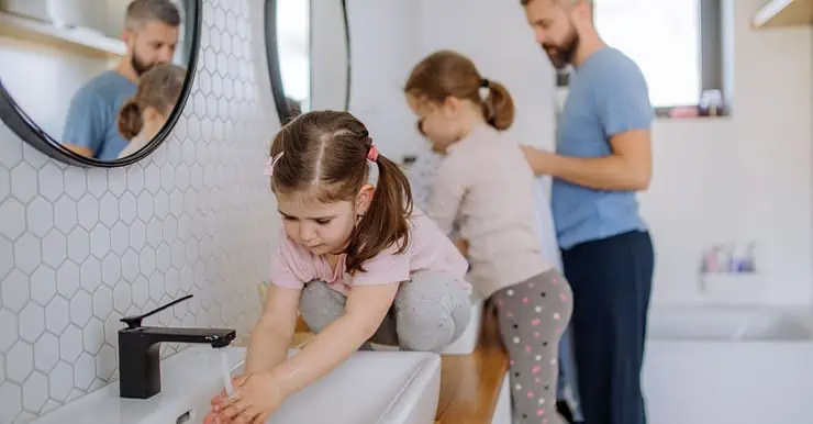 Un homme et deux petites filles se lavant les mains dans la salle de bain