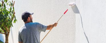 Un homme en casquette en train de peindre un mur extérieur avec un rouleau