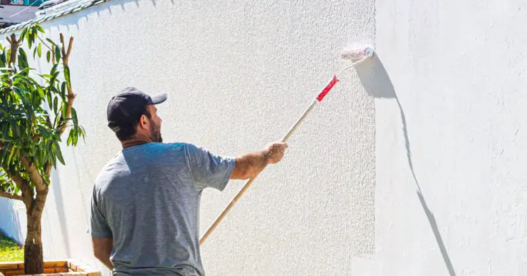 Un homme en casquette en train de peindre un mur extérieur avec un rouleau