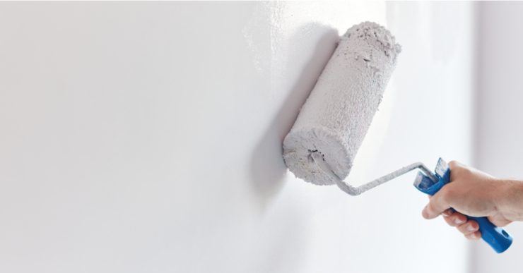 Main d'un homme en train de peindre un mur avec un rouleau de peinture