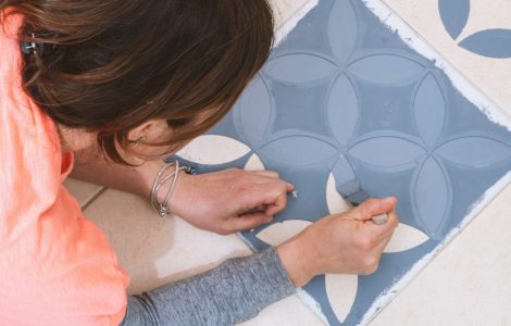 Une femme tenant une brosse pour peindre un modèle décoratif sur les carreaux de sol