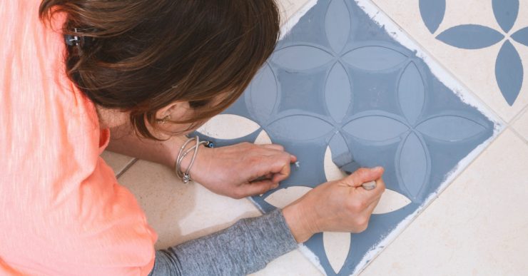 Une femme tenant une brosse pour peindre un modèle décoratif sur les carreaux de sol