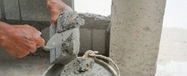Zoom sur les mains d’un homme mettant du ciment sur une brique pour construire un mur