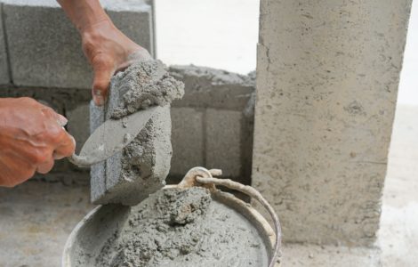 Zoom sur les mains d’un homme mettant du ciment sur une brique pour construire un mur