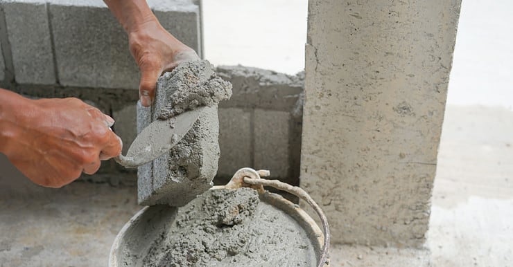 Zoom sur les mains d’un homme mettant du ciment sur une brique pour construire un mur