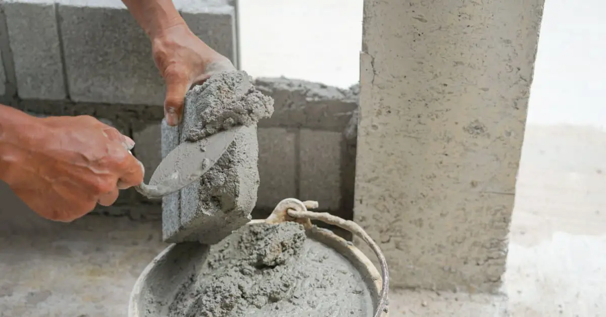 Zoom sur les mains d’un homme mettant du ciment sur une brique pour construire un mur