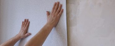 Des mains en train de tenir une bande de papier peint gris clair sur le mur