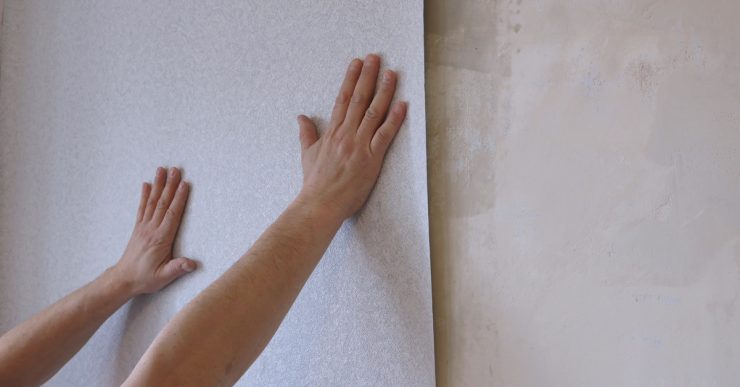 Des mains en train de tenir une bande de papier peint gris clair sur le mur