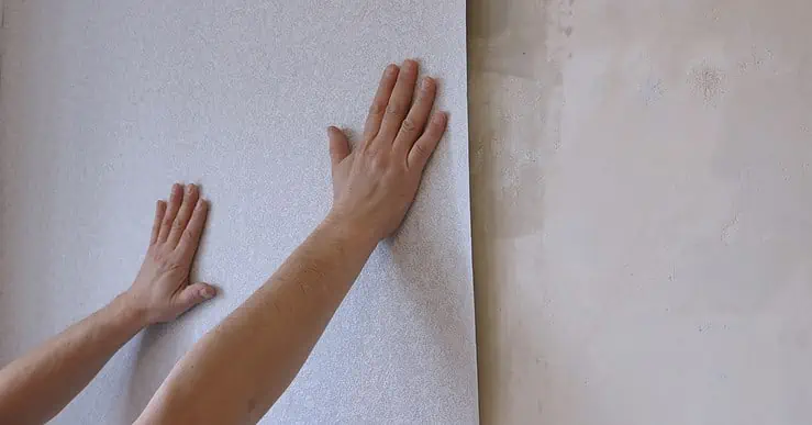 Des mains en train de tenir une bande de papier peint gris clair sur le mur