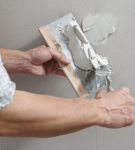 Un homme tenant une truelle comble les trous de vis sur un mur avec du plâtre