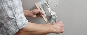 Un homme tenant une truelle comble les trous de vis sur un mur avec du plâtre