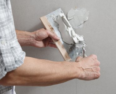 Un homme tenant une truelle comble les trous de vis sur un mur avec du plâtre