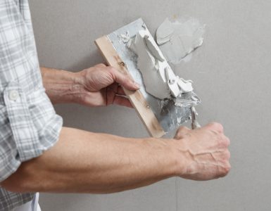 Un homme tenant une truelle comble les trous de vis sur un mur avec du plâtre