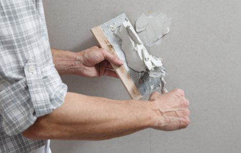Un homme tenant une truelle comble les trous de vis sur un mur avec du plâtre