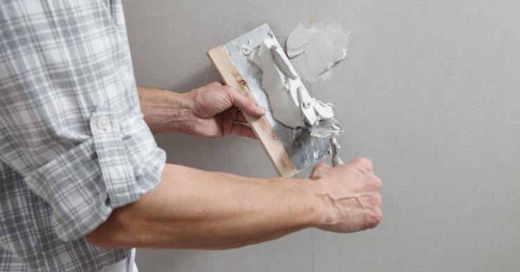 Un homme tenant une truelle comble les trous de vis sur un mur avec du plâtre