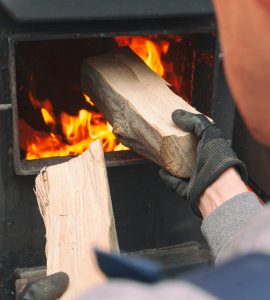 Un homme charge le bois de chauffage dans la chaudière allumée