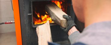 Un homme charge le bois de chauffage dans la chaudière allumée