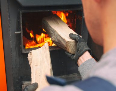 Un homme charge le bois de chauffage dans la chaudière allumée