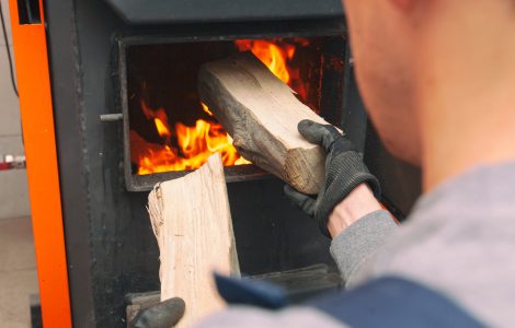 Un homme charge le bois de chauffage dans la chaudière allumée