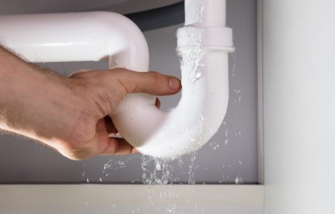 Main d'un homme tenant la fuite d'un tuyau d'évier blanc