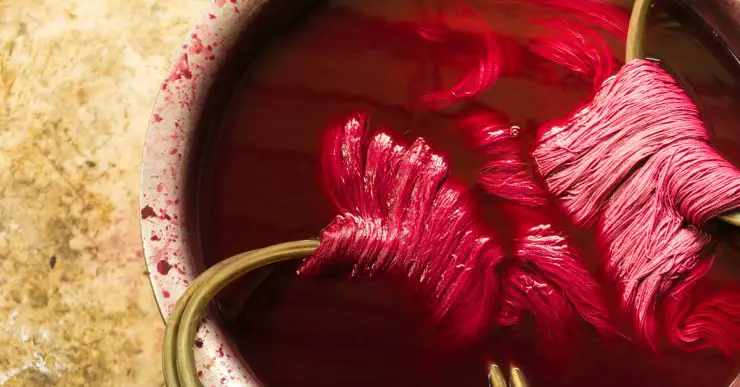 Fil de soie trempé dans un seau de teinture rouge