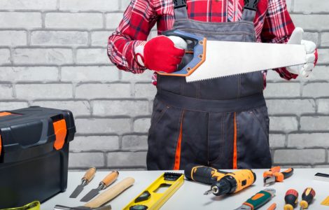 Un homme tenant une scie à main, et différents outils du bricoleur posés sur une table