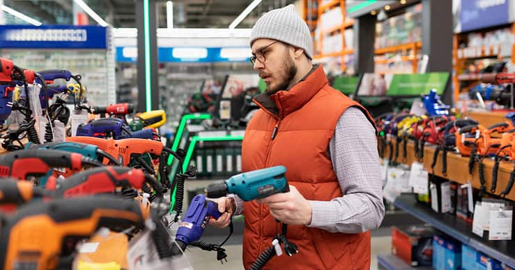 Un homme en train de choisir une perceuse dans un magasin