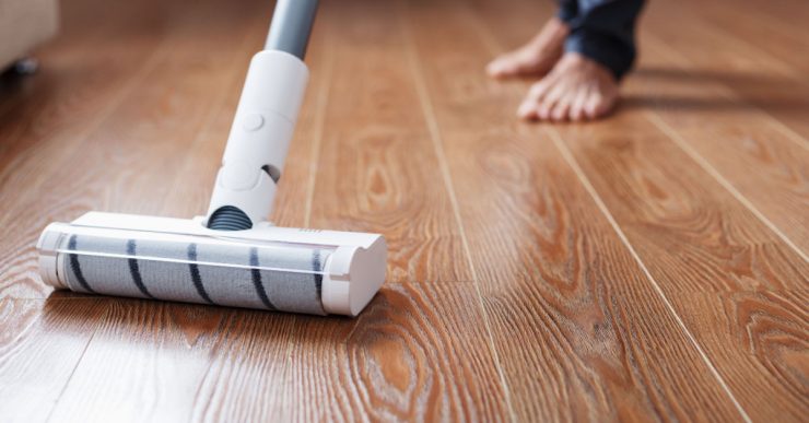 Une personne nettoie le parquet avec un aspirateur sans fil