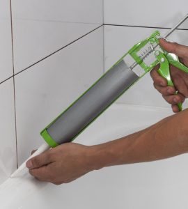 Une personne applique un joint en silicone autour de la salle de bain