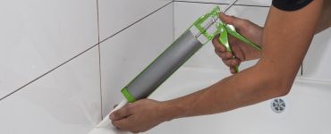 Une personne applique un joint en silicone autour de la salle de bain