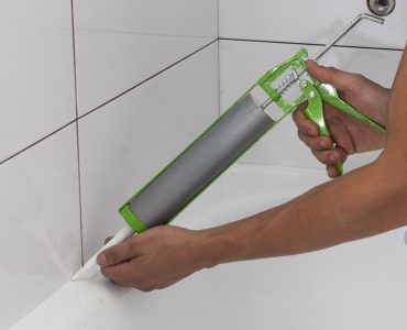 Une personne applique un joint en silicone autour de la salle de bain
