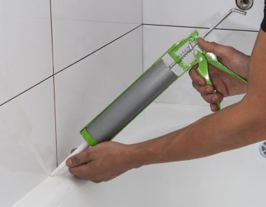 Une personne applique un joint en silicone autour de la salle de bain