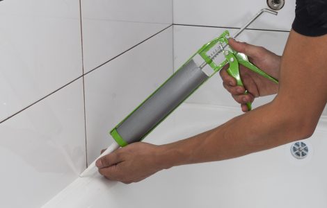 Une personne applique un joint en silicone autour de la salle de bain