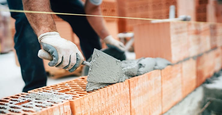 Un maçon en train de construire un mur en briques monomur