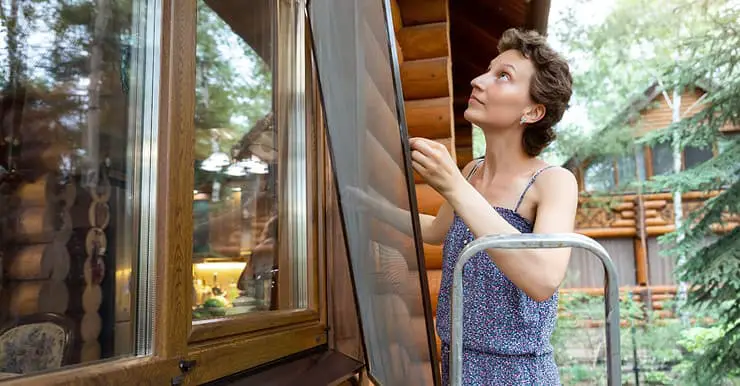 Une femme installe un moustiquaire sur sa fenêtre en bois vitrée