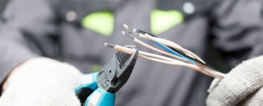 Focus sur les mains d’un électricien en train de dénuder un fil électrique avec une pince