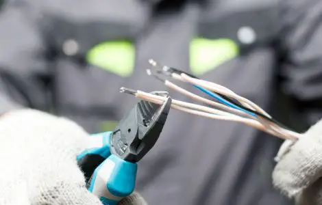 Focus sur les mains d’un électricien en train de dénuder un fil électrique avec une pince
