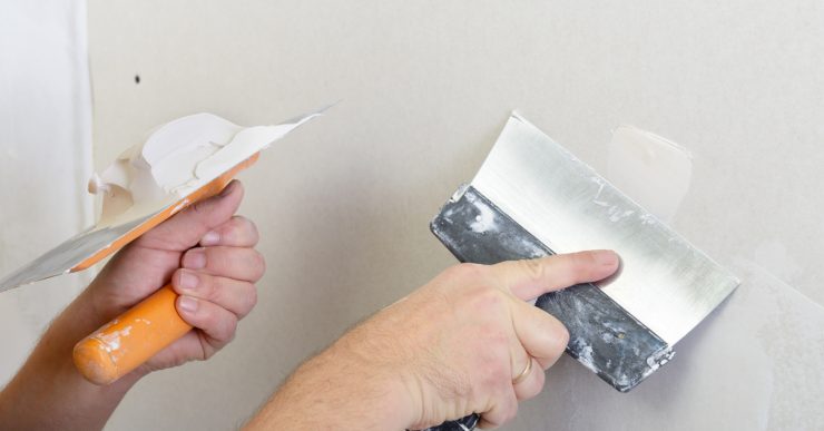 Gros plan sur les mains d'un homme rebouchant un trou sur le mur à l'aide de plâtre