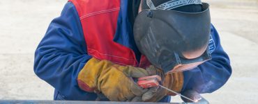 Un homme en combinaison bleu et rouge réalisant une soudure à l’arc électrique sur un tuyau